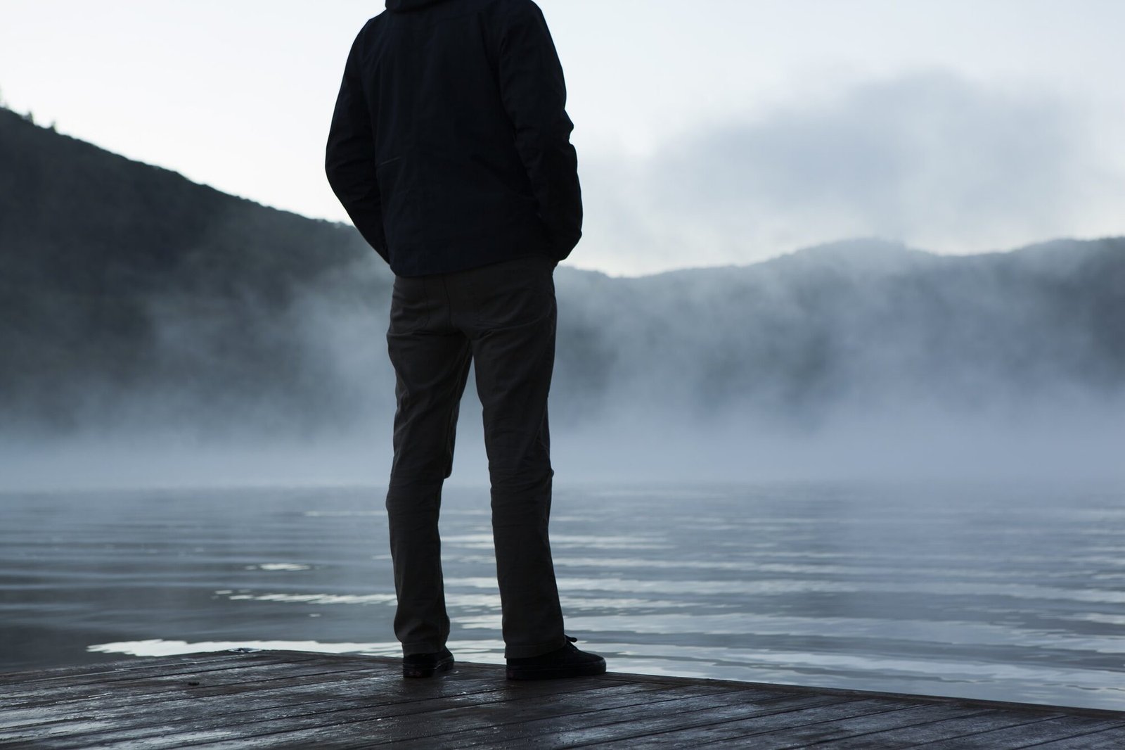 Un homme debout sur un ponton, face à un lac dans la brume.